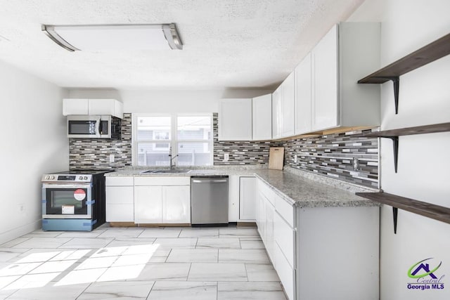 kitchen with sink, appliances with stainless steel finishes, white cabinetry, light stone countertops, and decorative backsplash