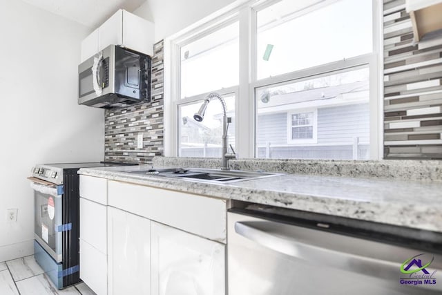 kitchen featuring sink, appliances with stainless steel finishes, backsplash, light stone counters, and white cabinets