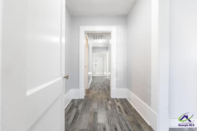 corridor with a textured ceiling and dark hardwood / wood-style flooring