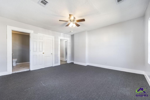 unfurnished bedroom with ceiling fan, connected bathroom, dark carpet, and a textured ceiling