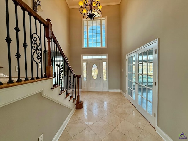 entrance foyer featuring ornamental molding, a towering ceiling, an inviting chandelier, and french doors