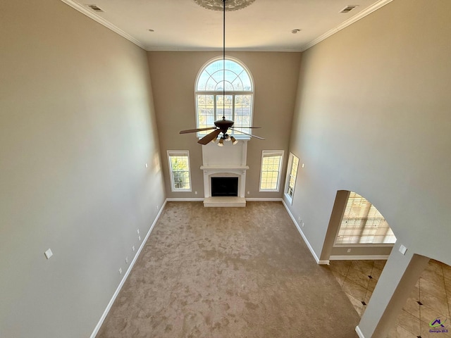 unfurnished living room featuring ceiling fan, light colored carpet, crown molding, and a towering ceiling