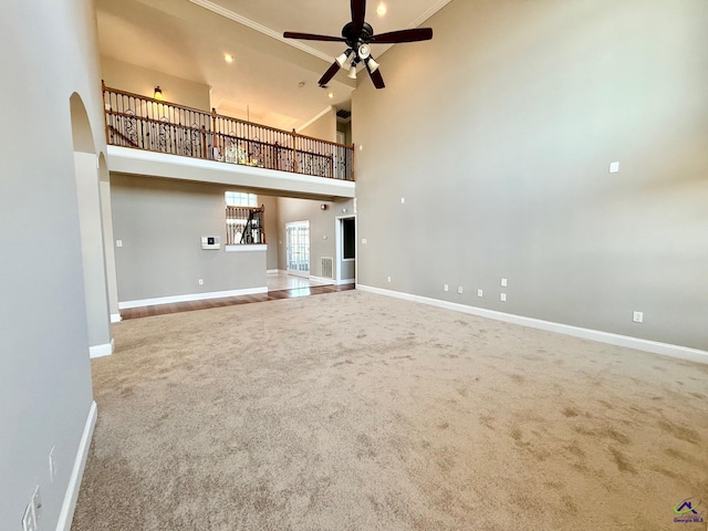 unfurnished living room featuring a high ceiling, carpet floors, and ceiling fan