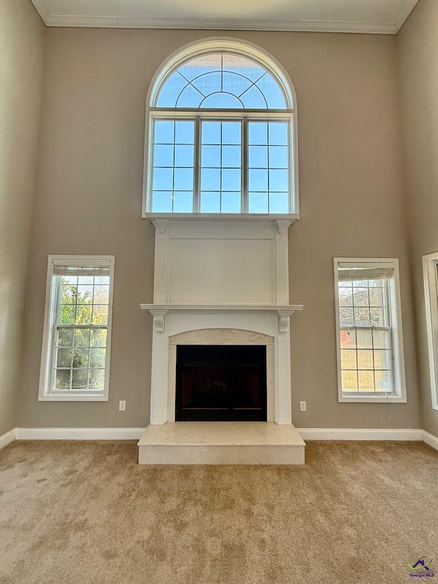 unfurnished living room with a premium fireplace, a towering ceiling, a wealth of natural light, ornamental molding, and light carpet