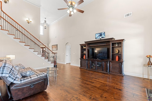 living room with dark wood-type flooring, ornamental molding, ceiling fan, and a high ceiling