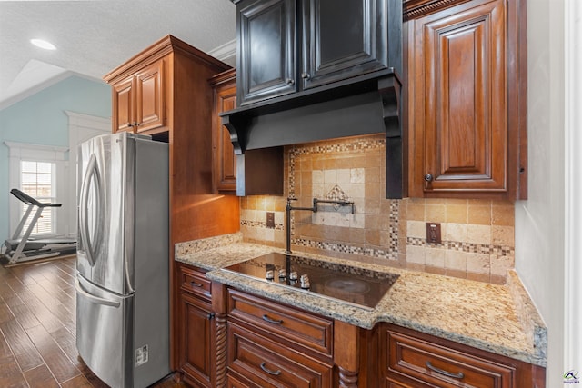 kitchen with dark wood-type flooring, light stone counters, tasteful backsplash, stainless steel refrigerator, and black stovetop