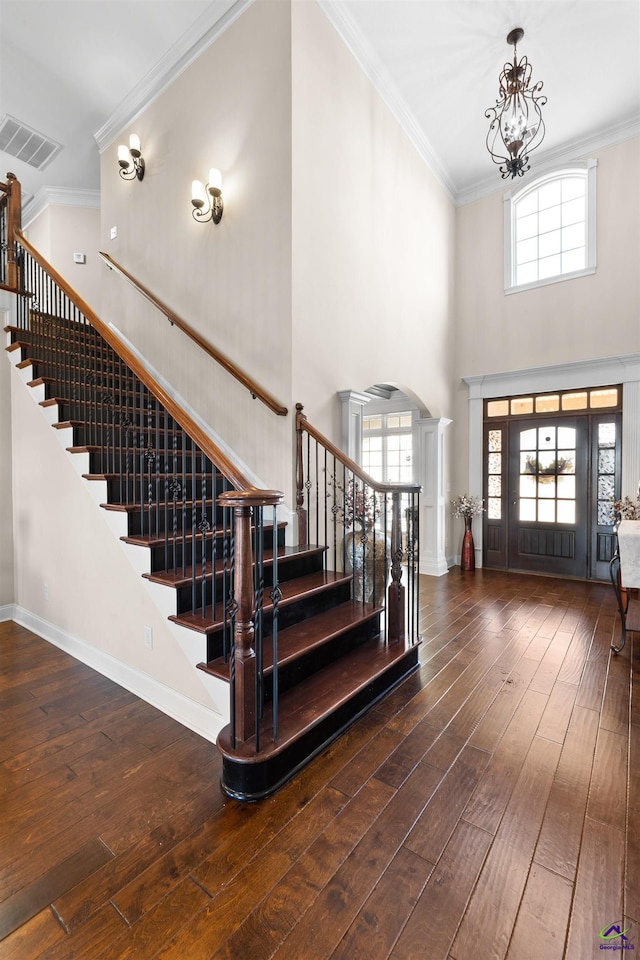 foyer entrance with crown molding, dark hardwood / wood-style flooring, an inviting chandelier, and ornate columns