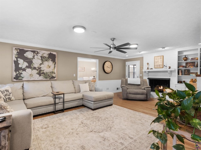 living room with crown molding, ceiling fan, hardwood / wood-style floors, and a brick fireplace