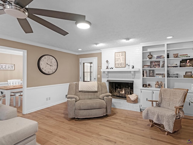 living room featuring crown molding, a brick fireplace, light hardwood / wood-style flooring, built in features, and ceiling fan