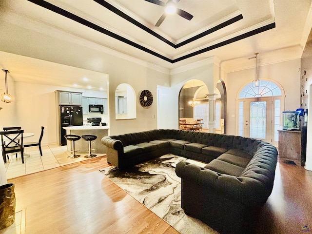 living room featuring ornamental molding, a tray ceiling, ceiling fan with notable chandelier, and light hardwood / wood-style flooring