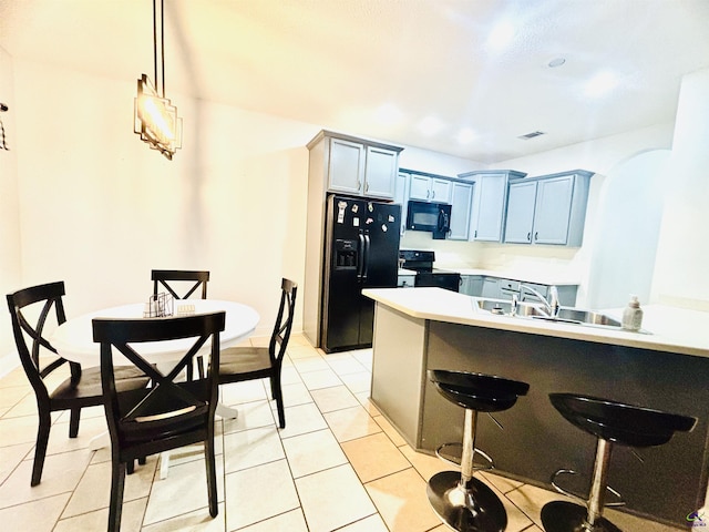 kitchen featuring pendant lighting, sink, black appliances, a kitchen bar, and light tile patterned flooring