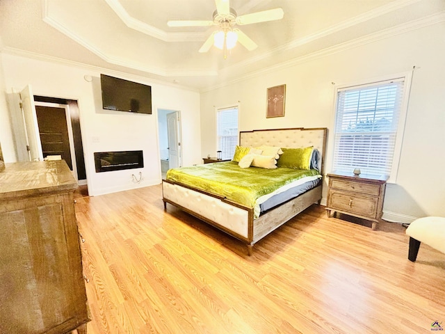 bedroom with ornamental molding, a raised ceiling, multiple windows, and light wood-type flooring