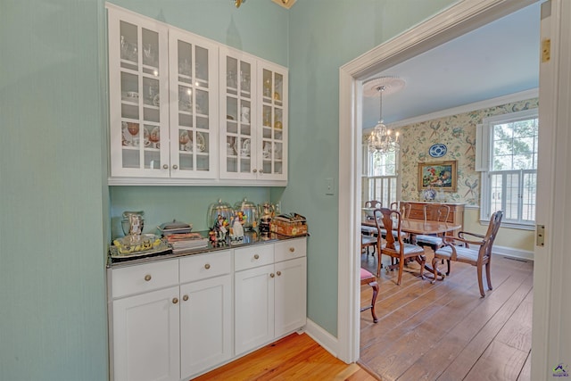 bar featuring decorative light fixtures, white cabinetry, ornamental molding, a notable chandelier, and light hardwood / wood-style flooring