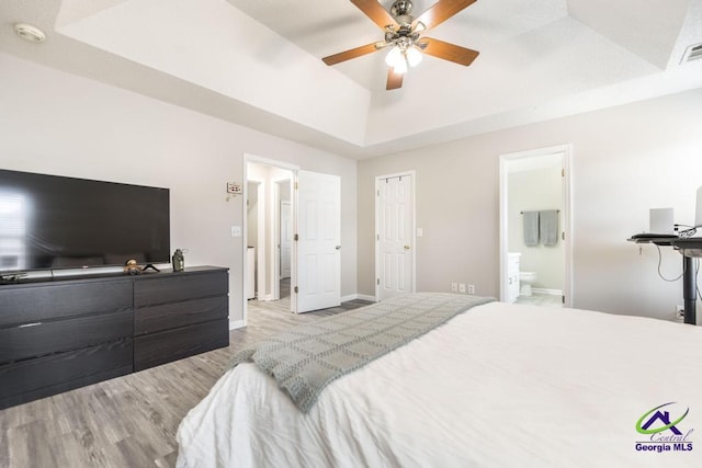 bedroom with ceiling fan, ensuite bathroom, a tray ceiling, and light hardwood / wood-style flooring