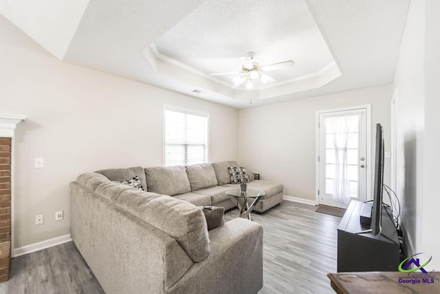 living room with ceiling fan, a tray ceiling, hardwood / wood-style floors, and a textured ceiling