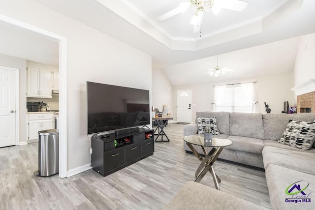 living room featuring ornamental molding, light hardwood / wood-style floors, a raised ceiling, and ceiling fan