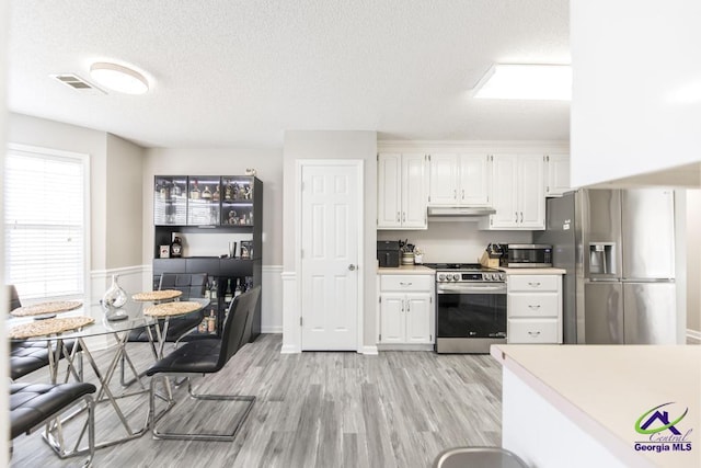 kitchen with a textured ceiling, stainless steel appliances, light hardwood / wood-style floors, and white cabinets