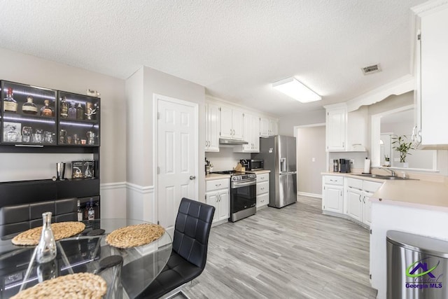 kitchen featuring sink, light wood-type flooring, white cabinets, stainless steel appliances, and a textured ceiling