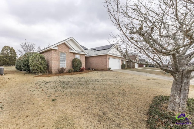 ranch-style home with a garage, a front yard, central AC unit, and solar panels