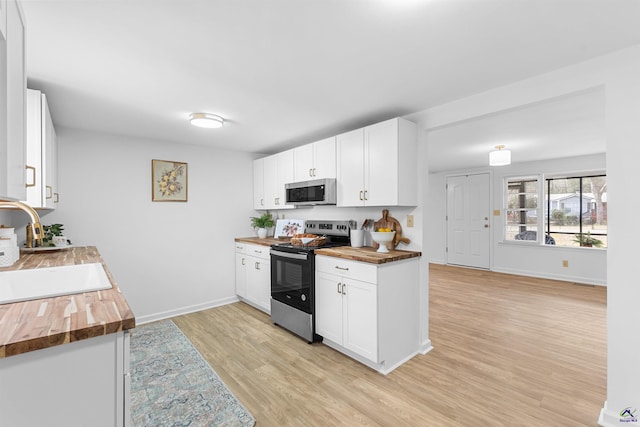 kitchen with butcher block countertops, sink, white cabinetry, stainless steel appliances, and light wood-type flooring