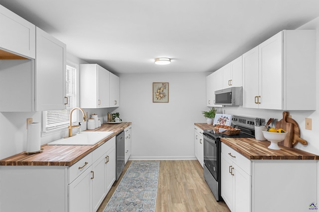 kitchen with sink, wooden counters, appliances with stainless steel finishes, white cabinetry, and light wood-type flooring