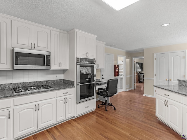 kitchen featuring appliances with stainless steel finishes, white cabinetry, backsplash, dark stone countertops, and light hardwood / wood-style floors