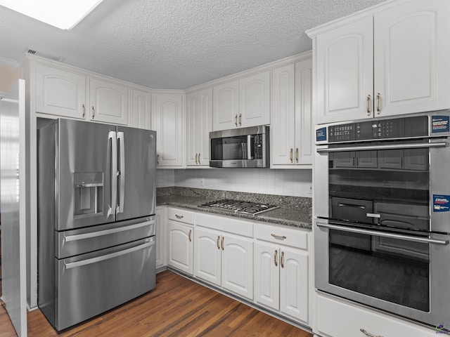 kitchen featuring appliances with stainless steel finishes, dark hardwood / wood-style floors, white cabinetry, backsplash, and dark stone counters