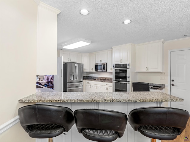 kitchen with a kitchen breakfast bar, stainless steel appliances, light stone countertops, white cabinets, and kitchen peninsula