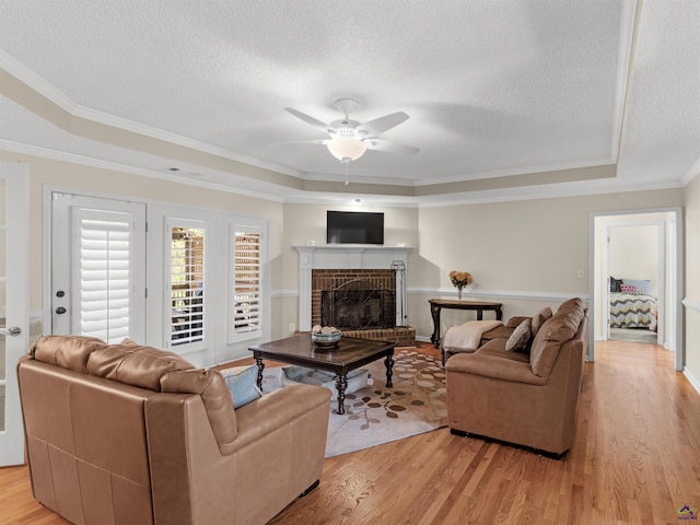 living room with light hardwood / wood-style flooring, ceiling fan, a tray ceiling, a fireplace, and ornamental molding