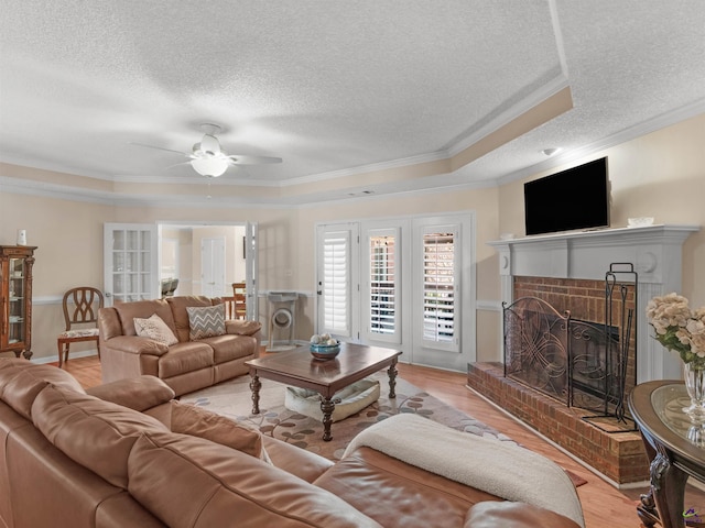 living room featuring light wood-type flooring, ornamental molding, a raised ceiling, a brick fireplace, and a textured ceiling