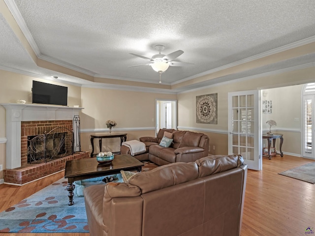 living room with a tray ceiling, a fireplace, crown molding, and light hardwood / wood-style flooring