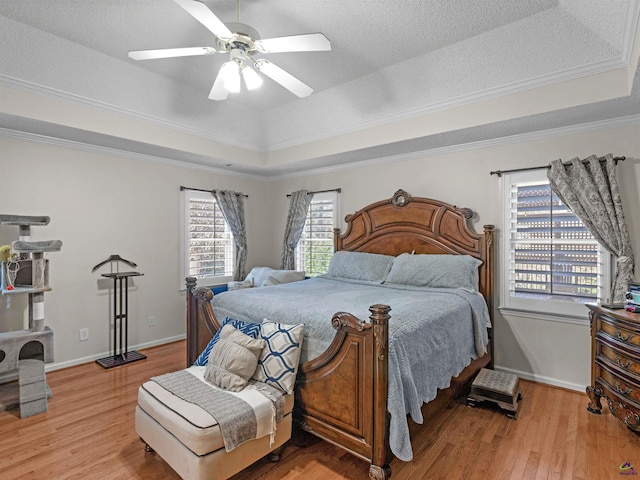 bedroom featuring crown molding, a tray ceiling, light hardwood / wood-style flooring, and a textured ceiling