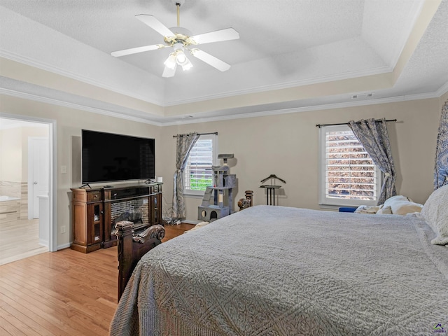 bedroom featuring wood-type flooring, ornamental molding, ceiling fan, and a tray ceiling