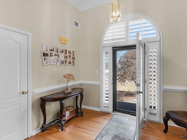 foyer entrance with crown molding, hardwood / wood-style floors, and an inviting chandelier