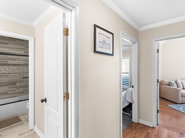 hall featuring ornamental molding, light hardwood / wood-style floors, and a textured ceiling