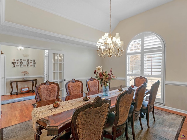 dining space with hardwood / wood-style flooring, ornamental molding, vaulted ceiling, and a notable chandelier