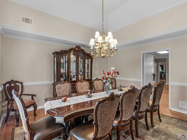 dining space with hardwood / wood-style flooring, crown molding, and a notable chandelier