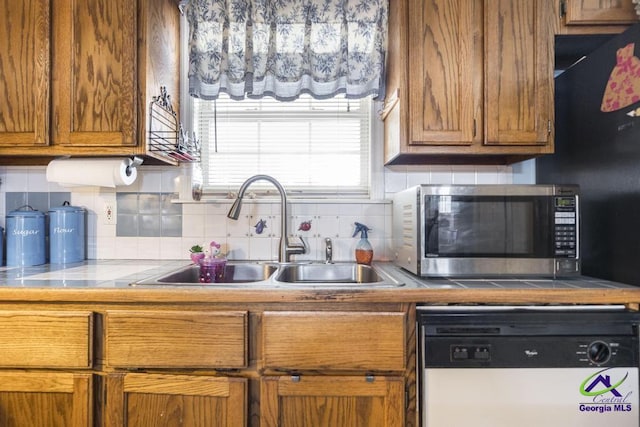 kitchen featuring white dishwasher, sink, decorative backsplash, and tile counters