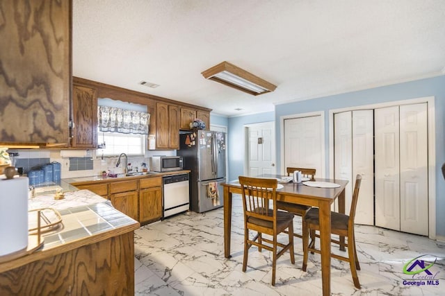 kitchen with appliances with stainless steel finishes, tile countertops, sink, backsplash, and crown molding