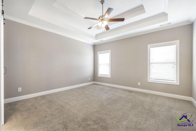 empty room with a raised ceiling, ornamental molding, carpet, and ceiling fan