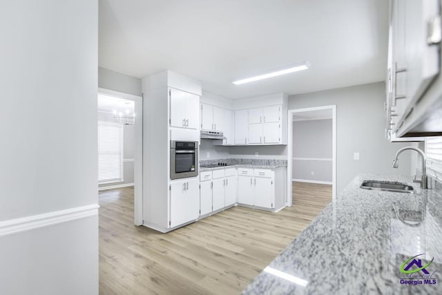 kitchen featuring sink, light hardwood / wood-style flooring, a notable chandelier, oven, and white cabinets