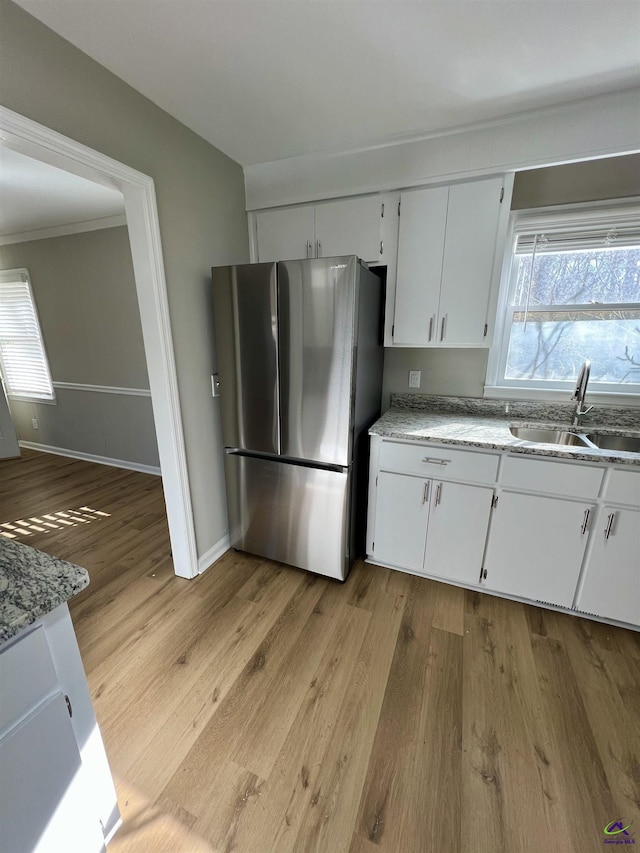 kitchen with stainless steel refrigerator, sink, white cabinets, light stone countertops, and light hardwood / wood-style flooring