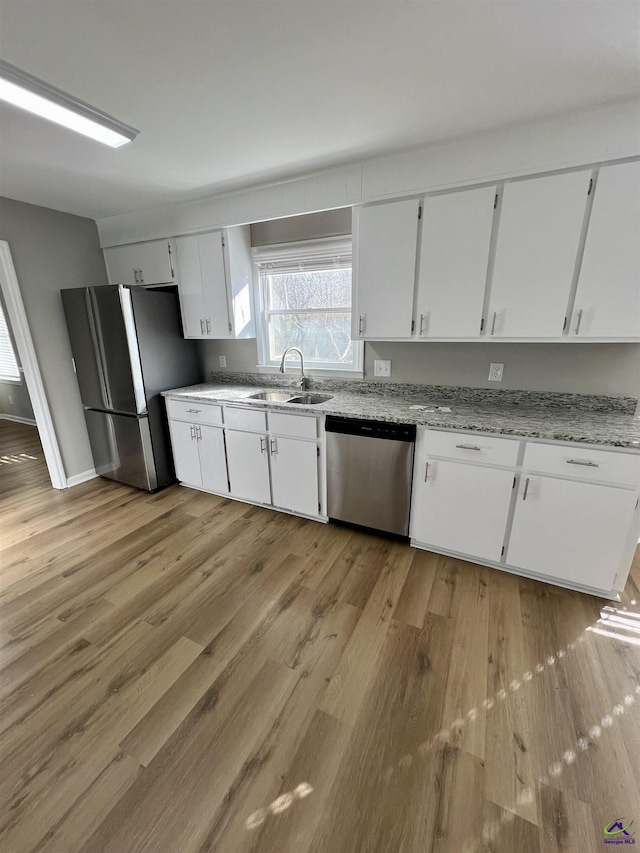 kitchen featuring sink, white cabinetry, appliances with stainless steel finishes, light stone countertops, and light hardwood / wood-style floors