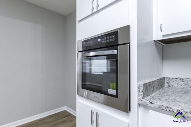 kitchen with oven, dark wood-type flooring, white cabinets, and light stone counters