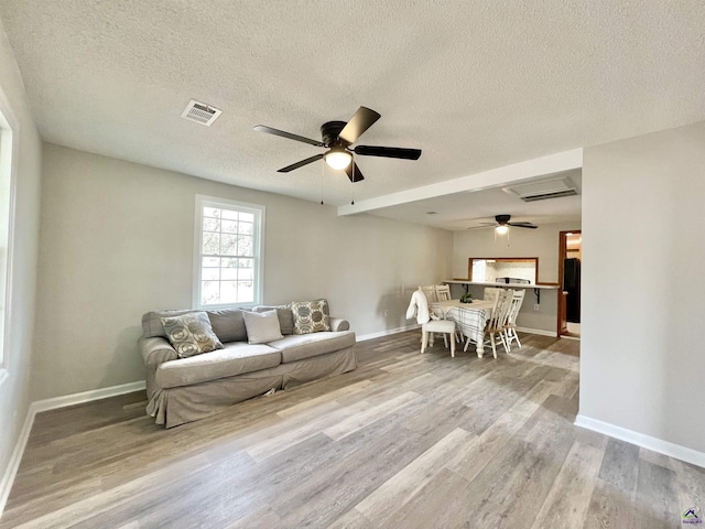 living room with ceiling fan, a textured ceiling, and light wood-type flooring