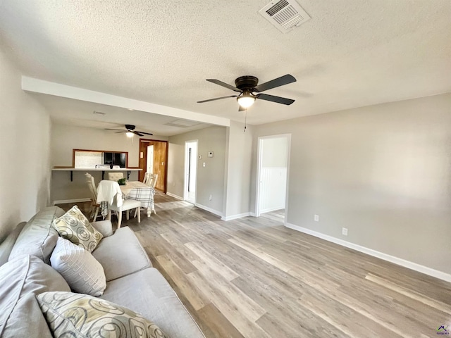 living room with ceiling fan, light hardwood / wood-style flooring, and a textured ceiling