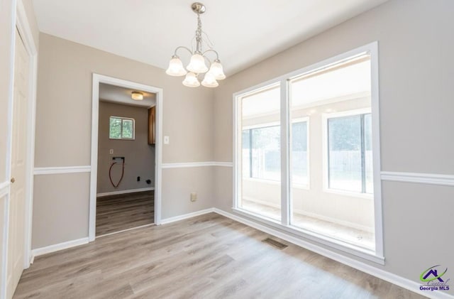 unfurnished dining area featuring a chandelier and light hardwood / wood-style flooring