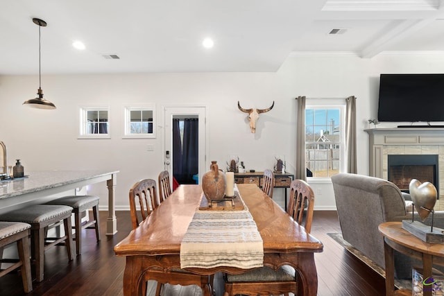 dining space with beamed ceiling, dark hardwood / wood-style flooring, and a tile fireplace