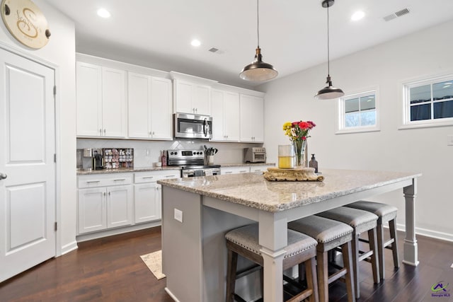 kitchen with light stone counters, decorative light fixtures, appliances with stainless steel finishes, an island with sink, and white cabinets