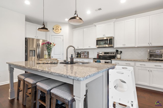 kitchen featuring hanging light fixtures, stainless steel appliances, white cabinets, and a center island with sink